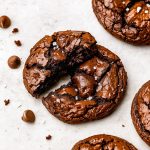 Stack of fudgy brookies with crackled tops and gooey centers, sprinkled with sea salt, on parchment paper.
