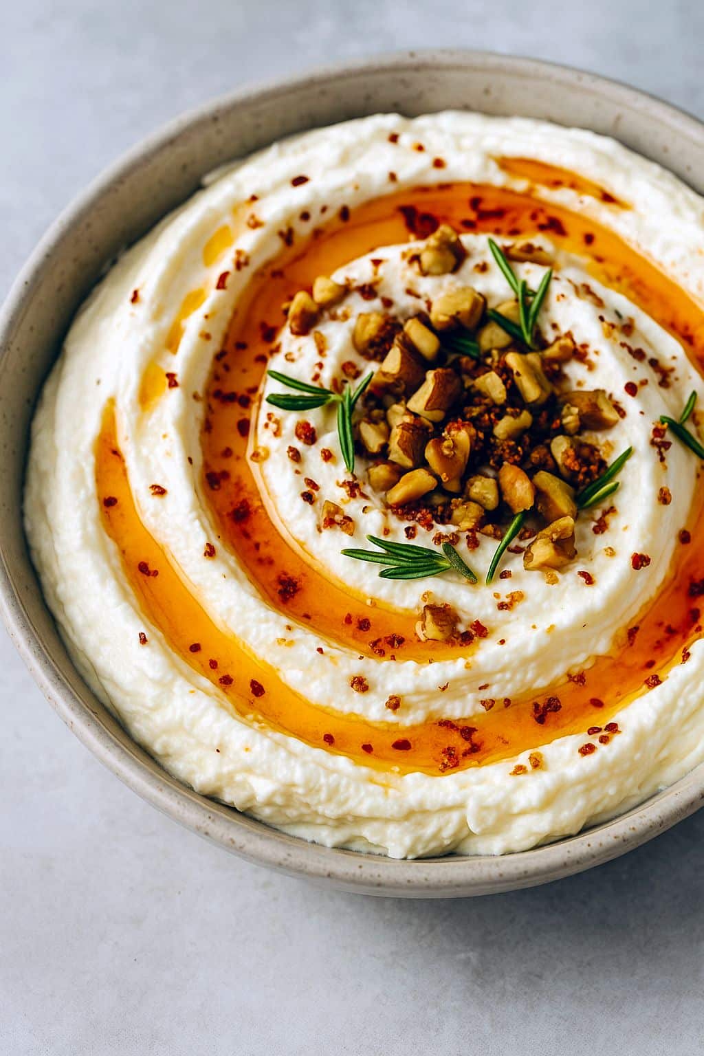 Close-up of Spicy Ricotta Dip topped with hot-honey drizzle, chopped walnuts, and rosemary, served on toasted crostini — a perfect Crostini Dip Recipes photo for August Appetizers boards.