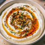 Close-up of Spicy Ricotta Dip topped with hot-honey drizzle, chopped walnuts, and rosemary, served on toasted crostini — a perfect Crostini Dip Recipes photo for August Appetizers boards.